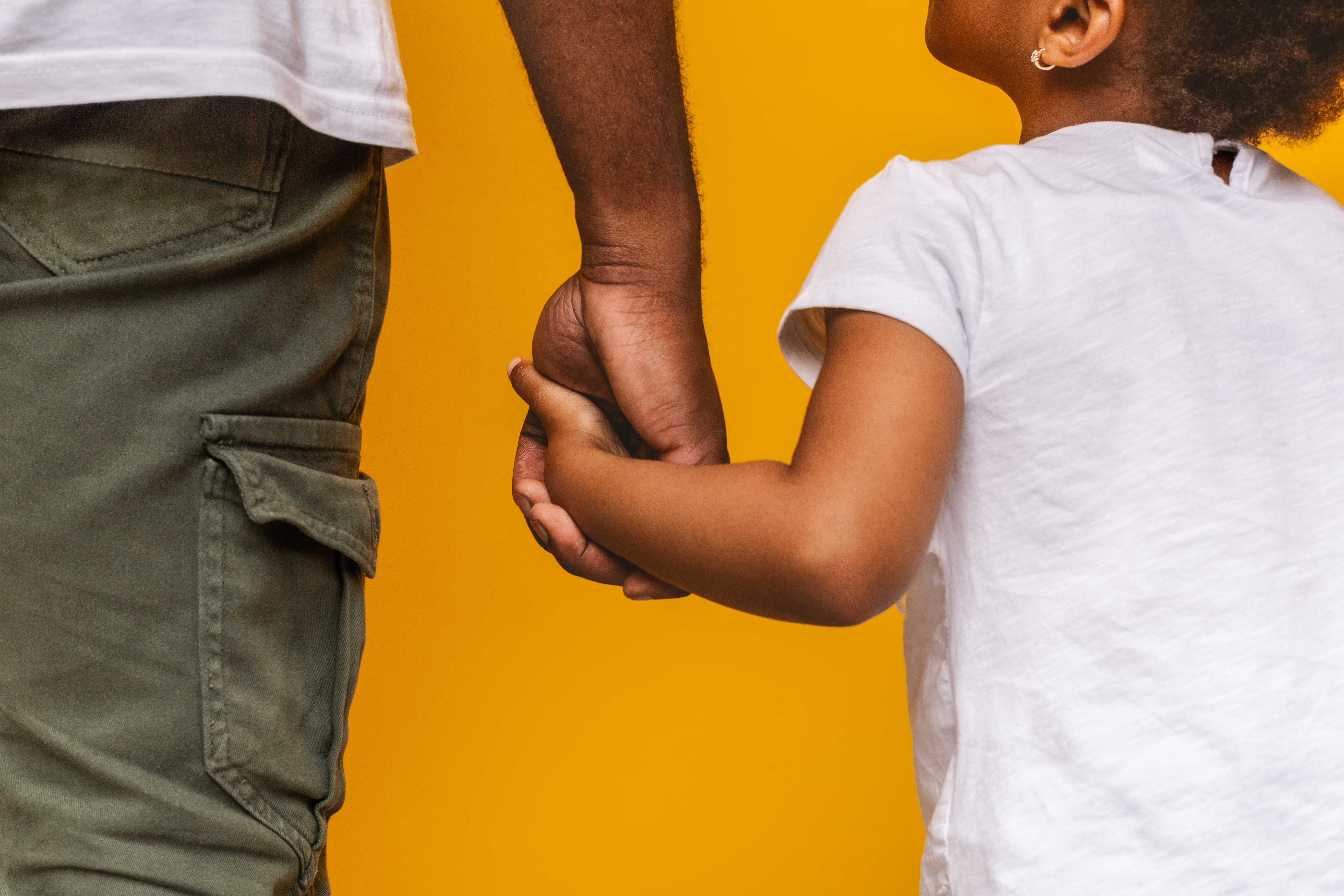 Absolute trust. Little african girl holding her daddy hand and looking at him, orange background